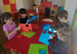 Dzieci siedzą przy stoliku i wypychają kolorowe figury geometryczne